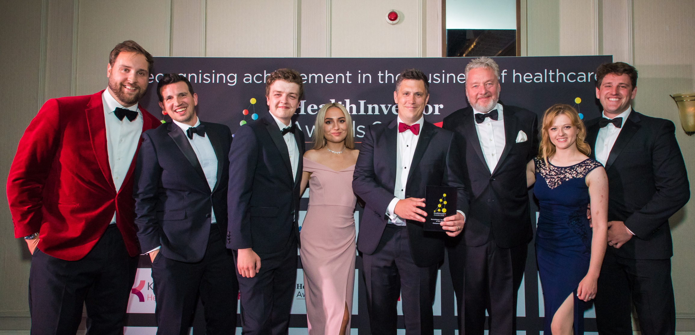 Compass Carter Osborne - A group of well-dressed CCO team members posing together at the HealthInvestor Awards. The individuals are wearing formal attire, with some holding an award. The background features a banner that reads "HealthInvestor Awards" and "Recognising achievement in the business of healthcare."